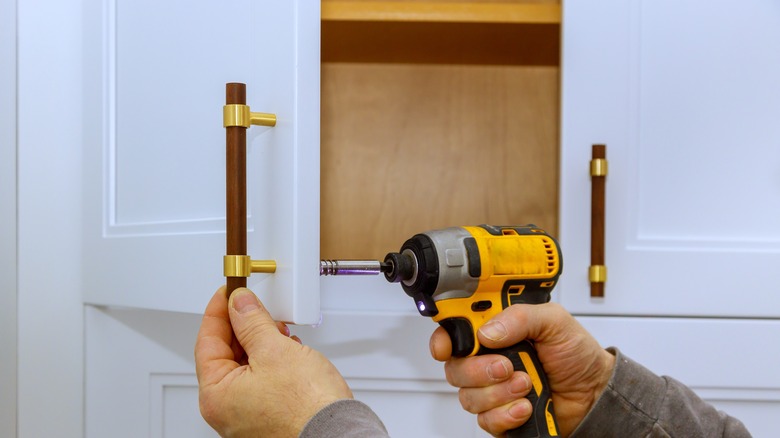 Vertical wooden pull with gold trim being attached to white kitchen cabinet