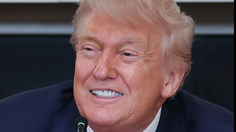 Donald Trump wears a blue suit and smiles at an event