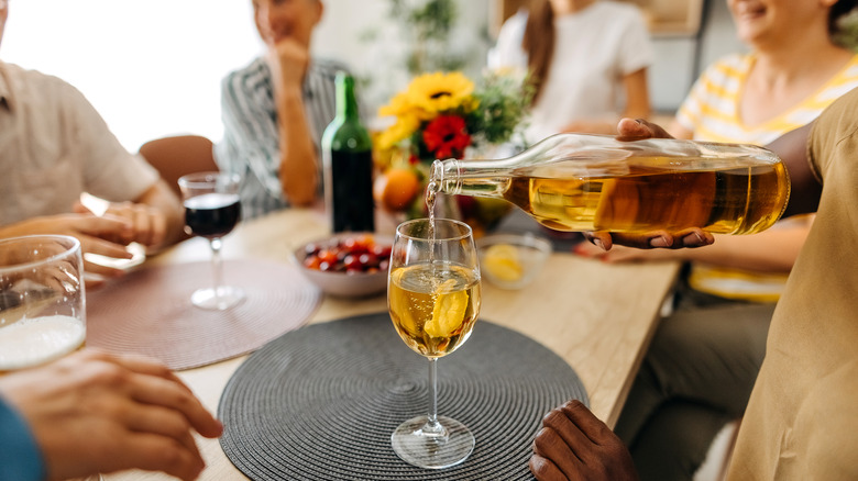 person pours wine for group of friends at table