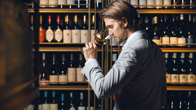 Person smelling wine in glass in front of shelves of wine