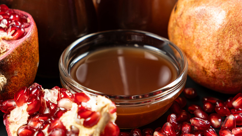 A small bowl of pomegranate molasses with fresh pomegranates
