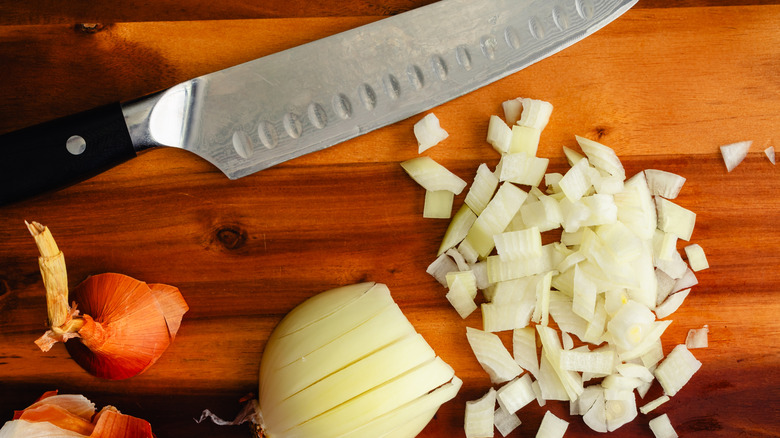 Diced onion on a wooden cutting board with a chef's knife and peels on the side