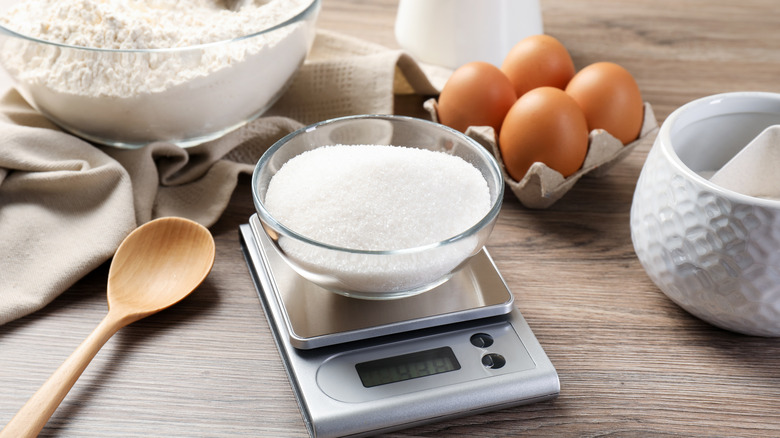 Digital kitchen scale with bowl of sugar and baking ingredients on wooden table