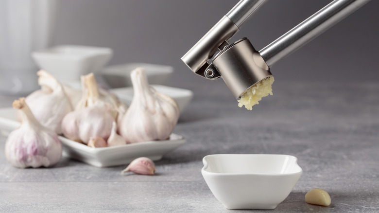 Garlic being squeezed with a garlic press into a small bowl