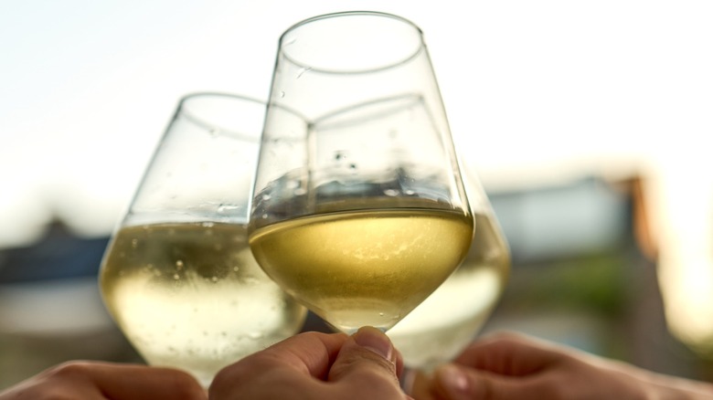Three hands making a toast with three glass of white wine.