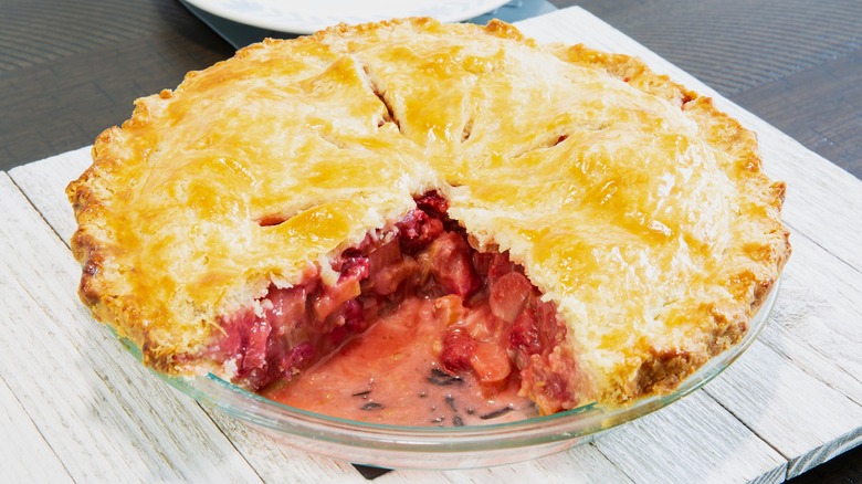 Strawberry rhubarb pie with slice missing on white wood table