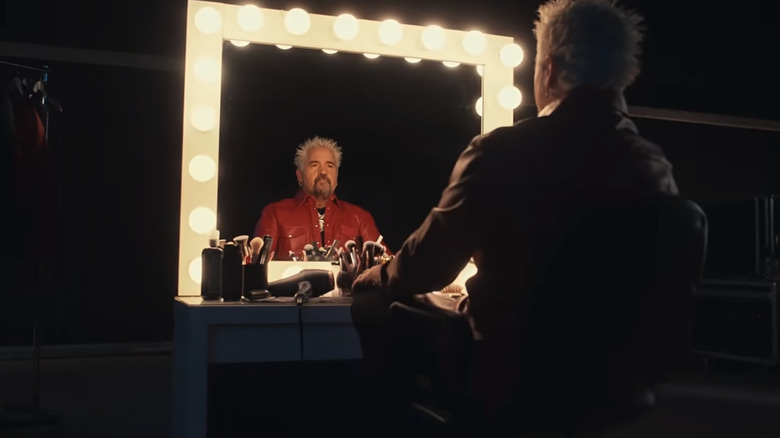 Guy Fieri in a red leather jacket sitting at a lighted vanity for a Bosch ad