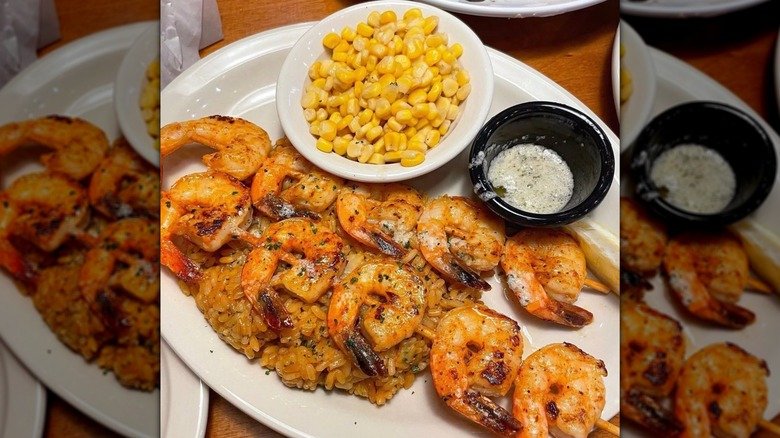 Texas Roadhouse grilled shrimp over rice with a side of corn on a white plate