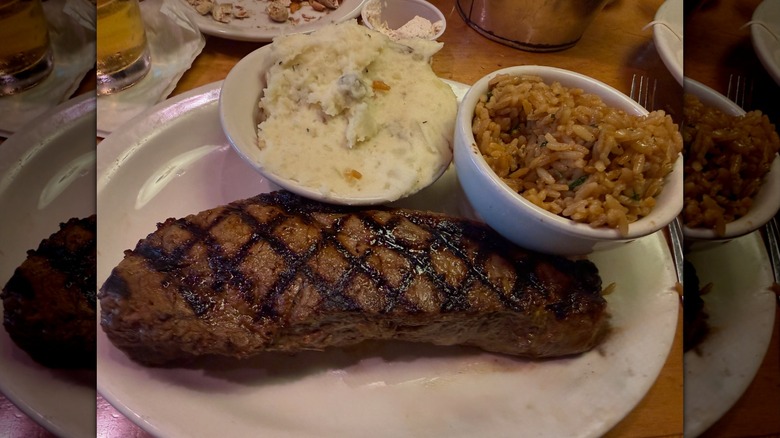 Texas Roadhouse New York Strip on a white plate with mashed potatoes and seasoned rice