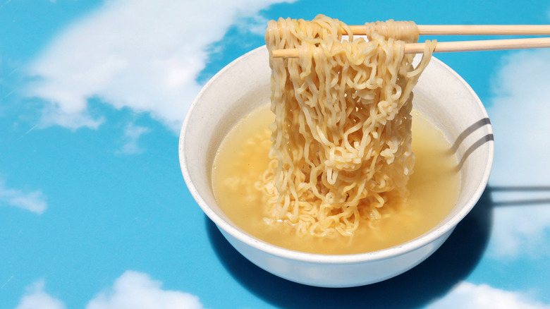 Chopsticks raise instant ramen in bowl against a background of blue skies