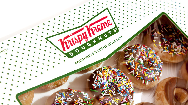 A white and green Krispy Kreme box full of different kinds of doughnuts