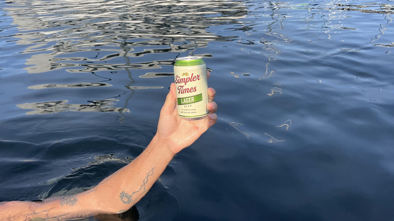 Hand holding a can of Simpler Times Lager above water