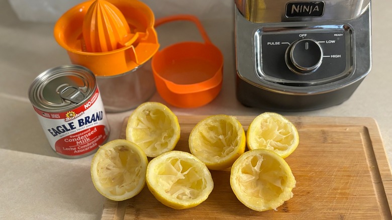 Sliced lemons on cutting board with blender and whipped lemonade ingredients