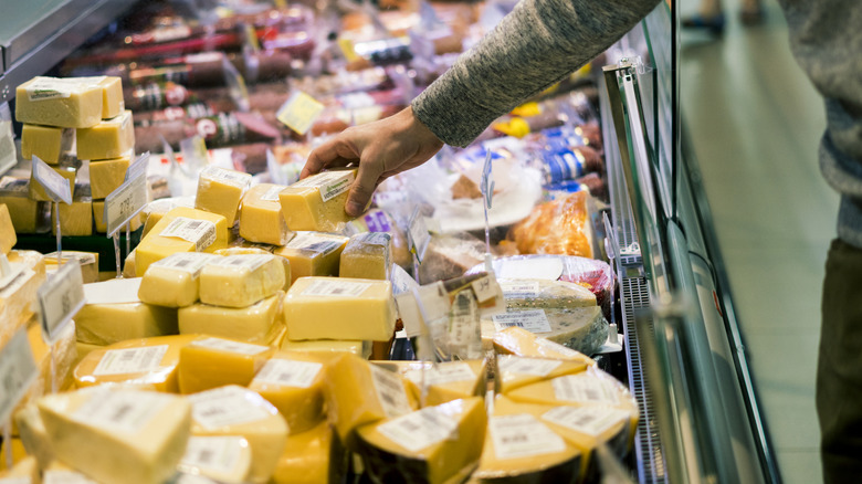 A shopper selects cheese from a grocery store display