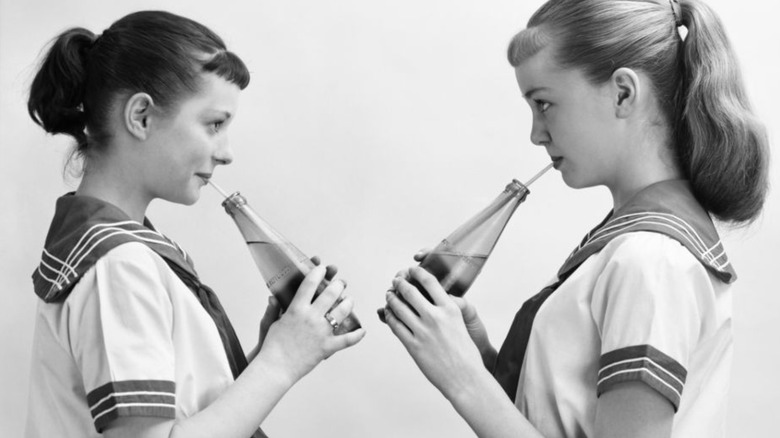 Black and white image of two girls drinking soda from bottles