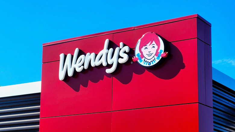 Wendy's all-white sign and logo on a red facade against a blue sky
