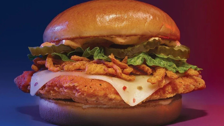 Fried chicken sandwich with melted white pepper jack cheese, lettuce, pickles, and crispy onions on a bun