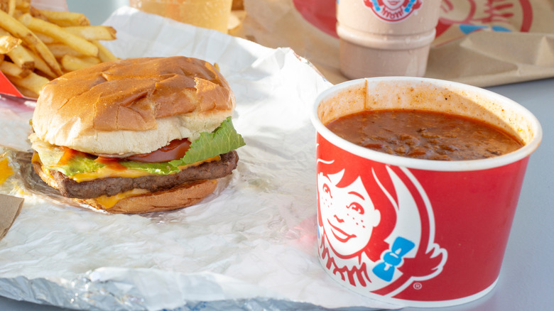A Wendy's burger next to a red cup of Wendy's chili, fries, and a milkshake