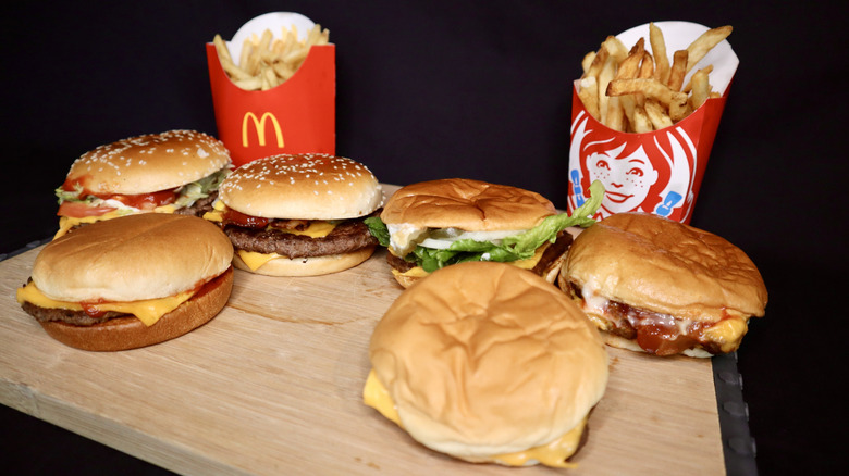 Six burgers and McDonald's and Wendy's fries on wooden board