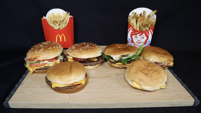 Six burgers and McDonald's and Wendy's fries on wooden board