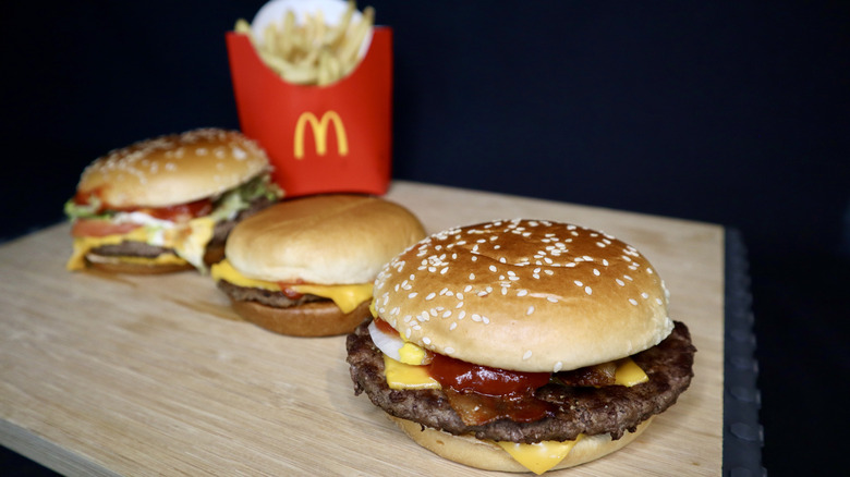Three burgers and McDonald's fries on wooden board