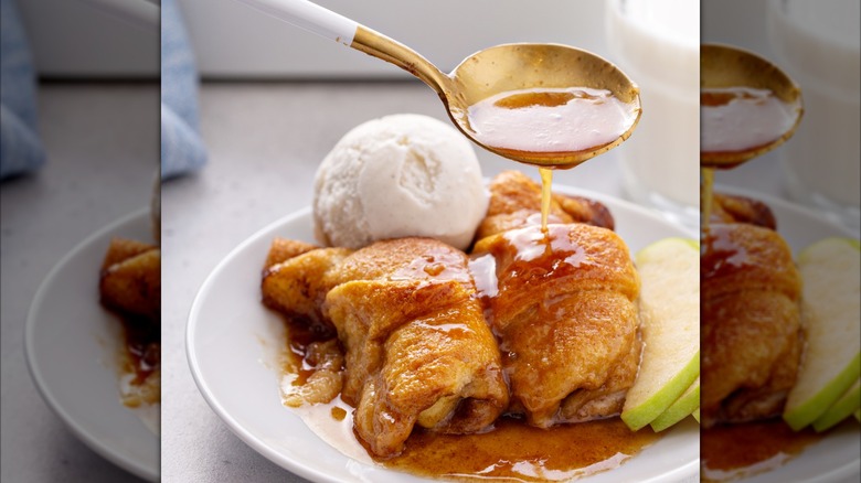 Two homemade baked apple dumplings being topped with a glaze with a scoop of vanilla ice cream beside it