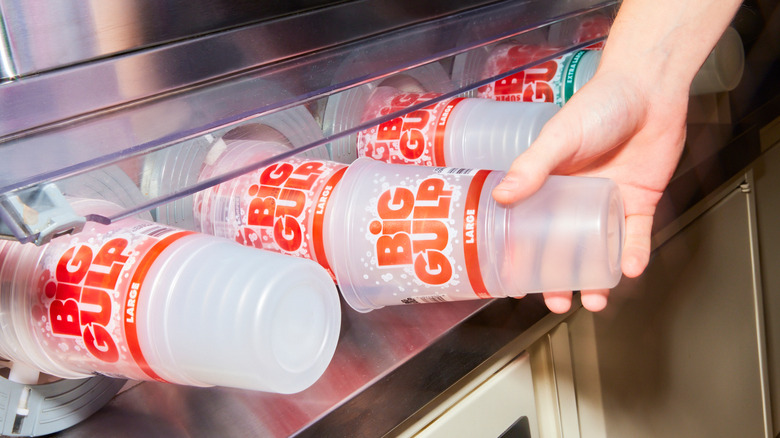 A hand reaches for a Big Gulp plastic cup
