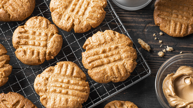 A cooling tray of peanut butter cookies with a glass bowl of peanut butter beside it