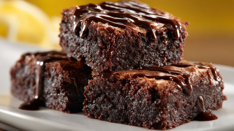 A tray of brownies piled and topped with a melted chocolate sauce