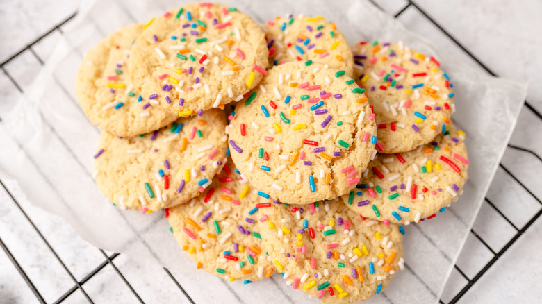 Sugar cookies with sprinkles sitting on a piece of parchment paper on a cooling rack