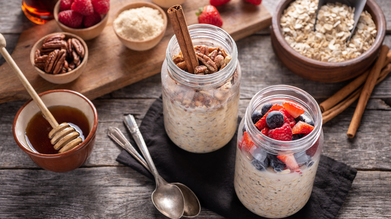 Jars of overnight oats with cinnamon sticks, honey, nuts, and berries