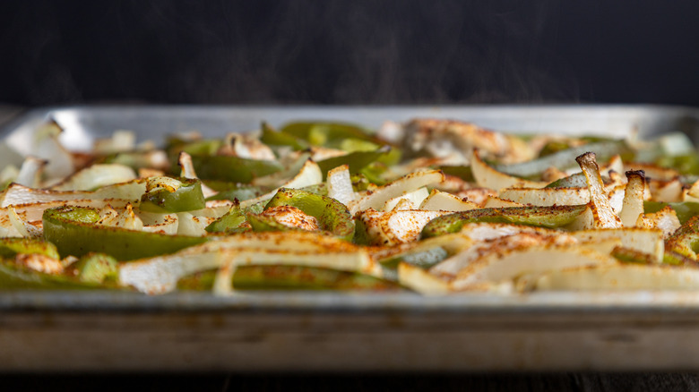 A sheet pan of chicken fajitas baking visible through an oven door