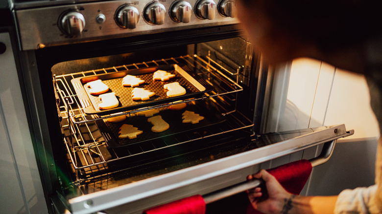 A woman checks two trays of sugar cookies in a convention oven