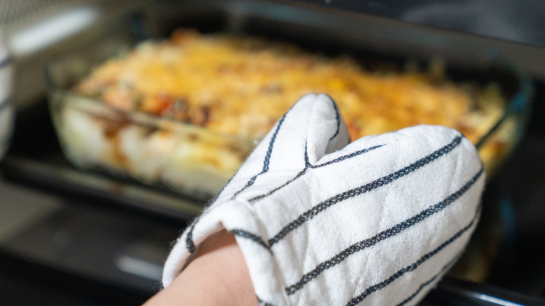 A hand in an oven mitt reaches into an oven to take out a casserole