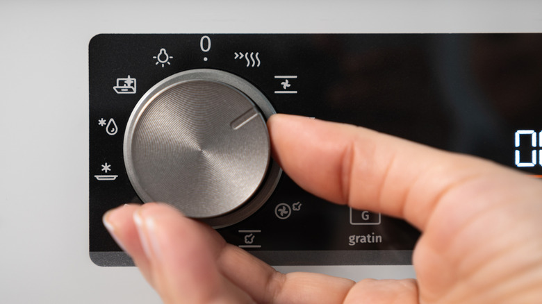 A person turning the kitchen oven knob to a setting