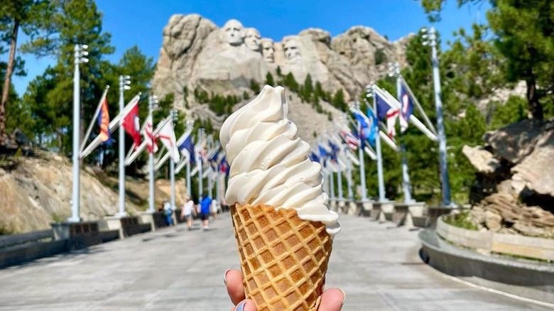 A hand holding an ice cream cone with Mount Rushmore in the background