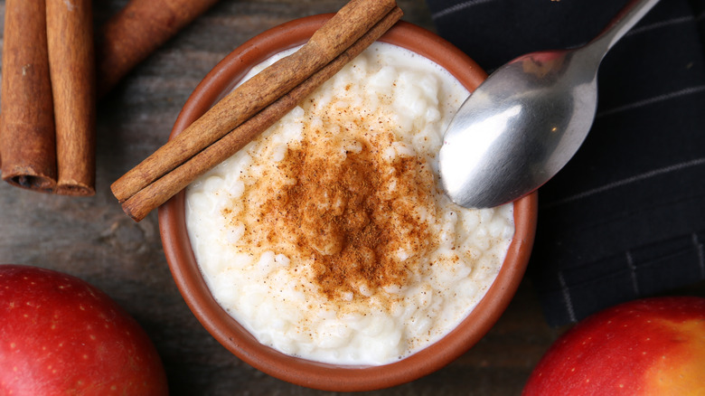 A bowl of rice pudding with cinnamon sticks and a spoon