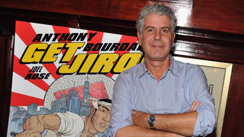 Anthony Bourdain posing in front of his graphic novel, "Get Jiro"