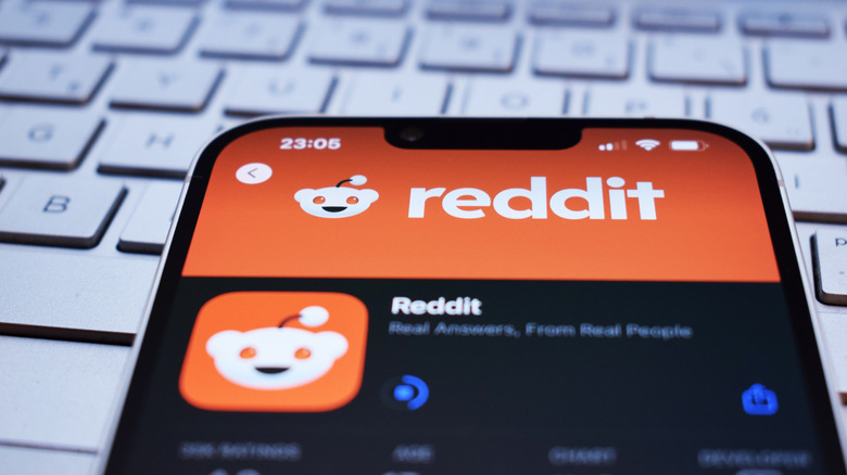 A phone showing a Reddit screen, lying on top of a keyboard