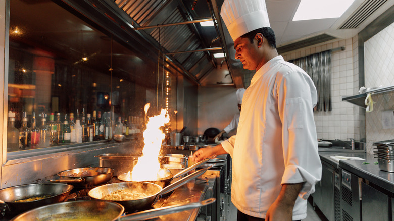 Chef handling multiple saute pans in restaurant kitchen