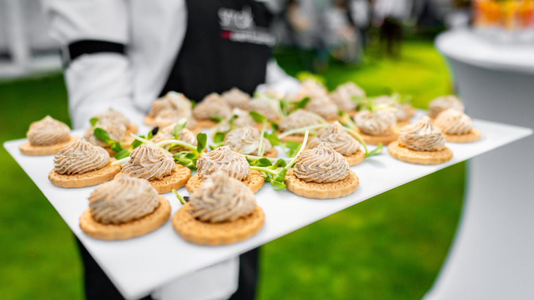 Canapés topped with whipped pâté being served on a platter by a waitress