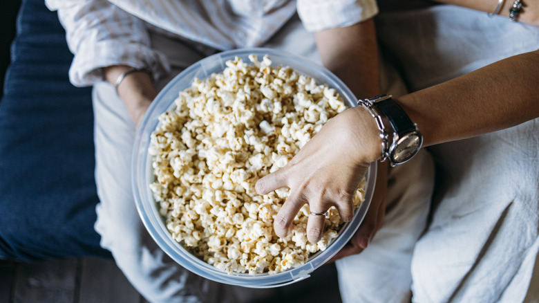 A couple takes turns reaching into a bowl of popcorn