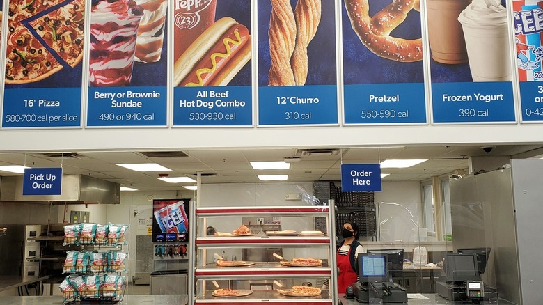 Sam's Club cafe counter with pizzas slices in heated display case beneath menu board