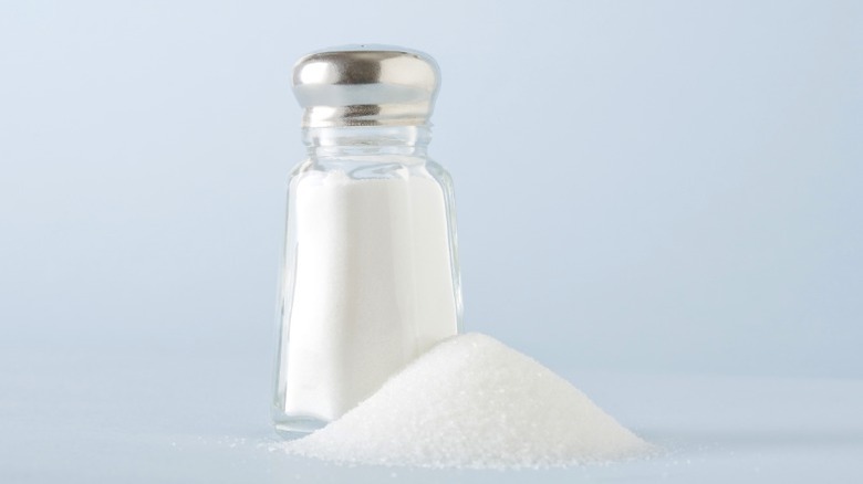 A small pile of salt next to a shaker.