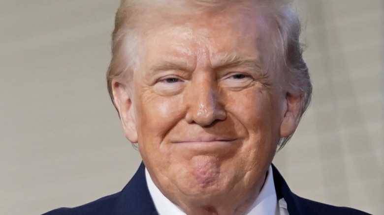 Donald Trump smirks in a blue suit jacket and white dress shirt