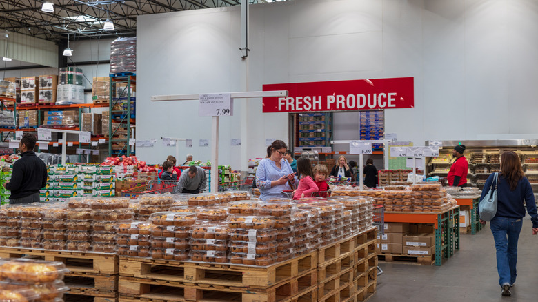 Several customers mill about the rows of baked goods in Costco.