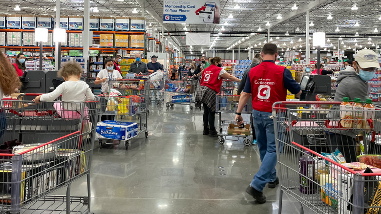 Employees and customers are standing in the self check-out aisle at Costco.