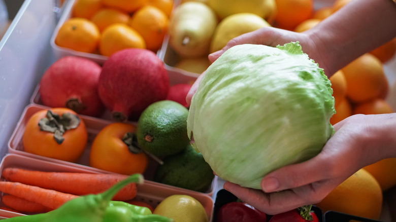 Hands holding a head of iceberg lettuce in produce section