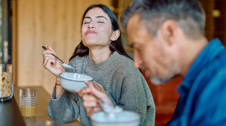 A woman eating yogurt out of a white bowl with her partner