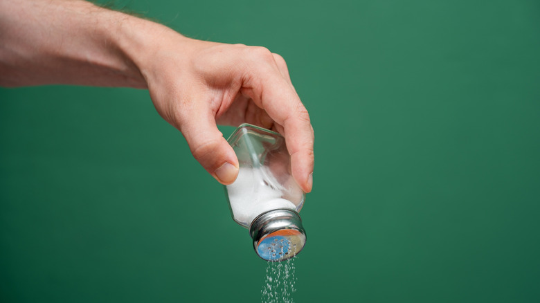 Hand shaking salt on a green background